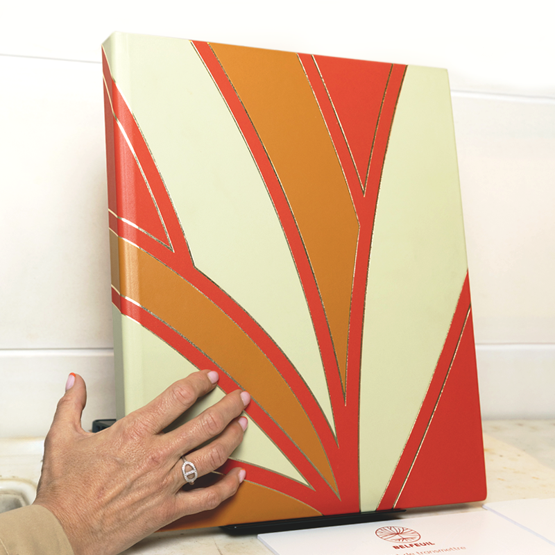 Livre Belfeuil en cuir Étincelle aux motifs rouge et ocre, posé sur son présentoir
